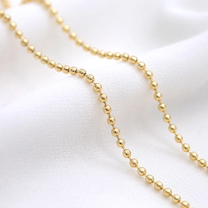 Polished 14K gold-plated 2mm ball chain for DIY necklace making on textured fabric