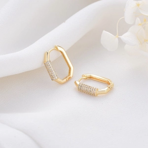 Pendientes geométricos bañados en oro 14K con circonitas sobre fondo de seda blanca