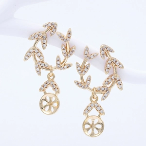 Détail des boucles d'oreilles dorées avec feuilles en zircone et pendentif floral évidé