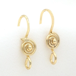 Macro shot of gold spiral drop earrings with a central metal sphere on a textured background