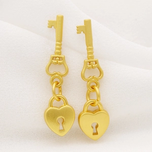 Macro shot of matte gold earrings with deer key design and heart-shaped lock detail