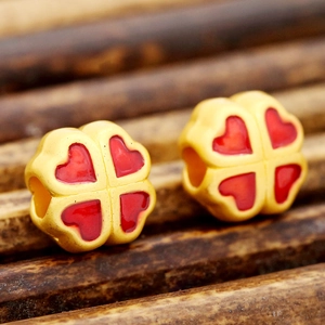 Vue macro de perles trèfle à quatre feuilles dorées avec cœurs en émail rouge pour bijoux