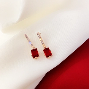 Close-up of gold earrings with rectangular red crystals on white satin and red backdrop
