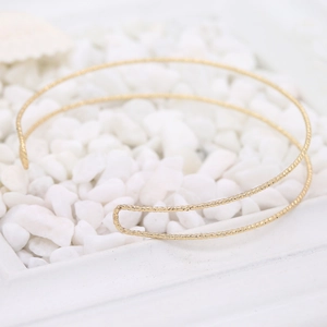 Minimalistischer goldener Choker mit gedrehter Struktur auf weißen Kieselsteinen