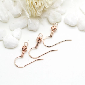Three rose gold DIY ball spring earring hooks displayed on white pebbles for jewelry making