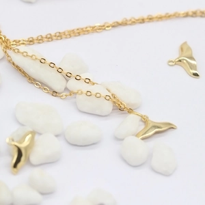 Detail van 14K vergulde dolfijnstaart hangers en ketting op witte decoratieve stenen