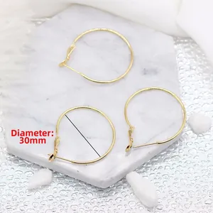 Détail des boucles d'oreilles créoles dorées 14K de 30mm sur marbre blanc