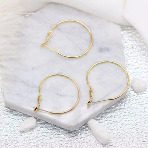 Boucles d'oreilles créoles minimalistes plaquées or 14K sur marbre blanc avec plumes