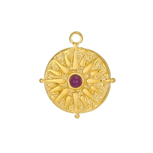 Macro detail of vintage sunburst pendant with red zircon inlay in textured gold plating