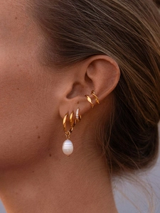 Close-up of stacked gold hoop earrings and pearl drop charms on model ear