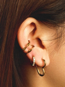 Detail of gold heart earrings and twisted cuffs set on model's ear with crystal accents