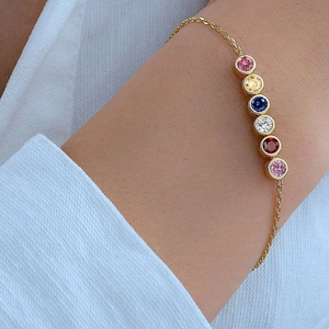 Golden bracelet on wrist with six colorful round birthstones in minimalist bezel settings