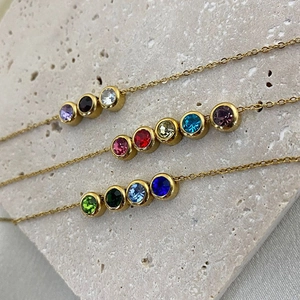 Macro detail of three rose gold chains with colorful birthstones on a textured stone surface