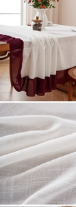 Close-up detail of white linen tablecloth featuring burgundy ruffled edges and mesh texture