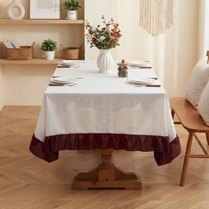 Minimalist cream linen tablecloth with burgundy ruffled edges on a wooden table