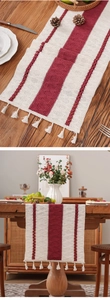 Detail of red and cream striped table runner with handmade tassels on wooden surface