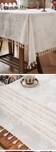 Detail of vintage beige floral jacquard tablecloth with elegant white handmade tassels