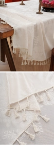 Close-up of beige jacquard tablecloth with floral relief patterns and woven tassel fringe