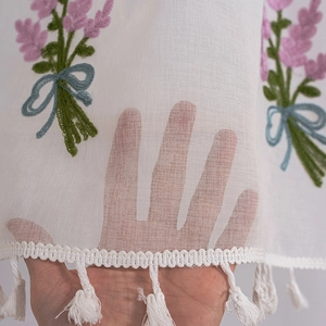 Detail of white lace cafe curtain with lavender embroidery and cotton tassel fringe