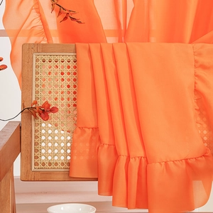 Elegant orange chiffon curtain featuring decorative ruffles on a vintage wooden chair