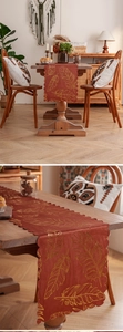 Detail of dark red table runner with golden feather patterns and wavy lace edges