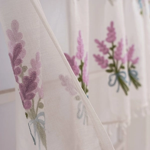 Close-up of lavender flower embroidery and blue bow on white lace cafe curtain fabric