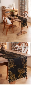 Detail of black velvet table runner with gold feather embroidery and wavy lace edges