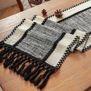 Bohemian black and white woven table runner with decorative tassels on a wooden table