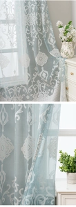 Detailed close-up of light blue lace curtain with white damask pattern and embroidery
