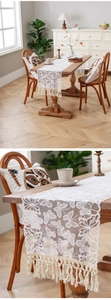 Detail of white lace table runner with hollow floral design and fringe edges on wood table