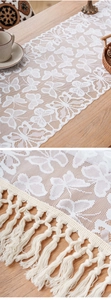 Detail of white lace table runner featuring crochet butterfly patterns and elegant long tassels