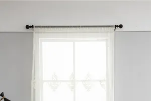 Detail view of white sheer curtain featuring vintage floral embroidery and black tassels