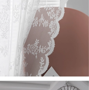 Macro shot of white lace curtain with intricate floral embroidery and wavy scalloped edges