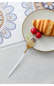 Detail of stainless steel fork with golden head and elegant white handle on tablecloth