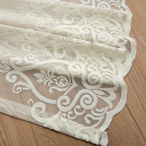 Elegant beige lace curtain with floral patterns and scalloped edges on wood floor