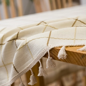 Minimalist beige checkered tablecloth with tassels on a wooden table, cotton linen texture