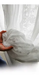 Close-up of white lace curtain fabric showing detailed floral embroidery patterns