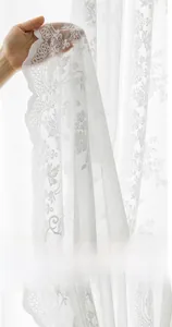 Detail of white lace curtain with delicate floral embroidery and semi-transparent texture