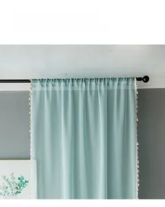 Detail of light blue linen texture curtain with white pom-pom fringe trim on black rod