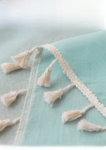 Detailed close-up of mint green linen fabric texture with decorative cream fringe
