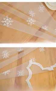 Détail de nappe en dentelle blanche avec broderie flocon et bordure festonnée sur bois