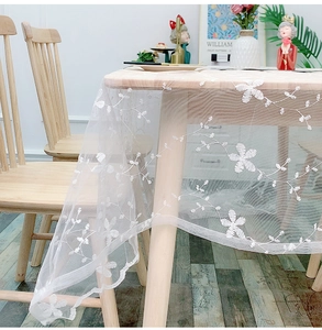 Detailed close-up of white floral lace tablecloth with embroidery on a dining table