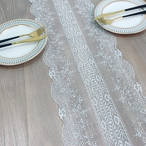 Elegant white lace table runner with vintage floral embroidery on grey wooden surface