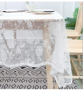 Detail of white lace tablecloth featuring intricate rose patterns on a wooden table