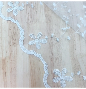 Detail of white floral embroidery lace on a rectangular mesh tablecloth with wavy edges