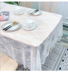 Close-up of white lace tablecloth with floral hollow patterns and wavy edges on a wooden table