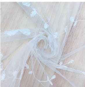 Detail of white lace mesh tablecloth with delicate floral embroidery on light wood background