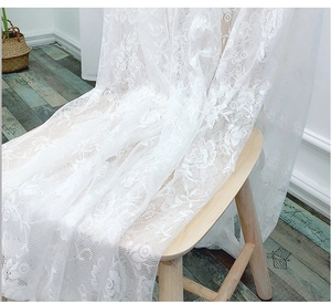 Close-up of white lace tablecloth featuring delicate rose floral patterns on a wooden chair