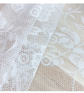 Detailed macro view of white floral lace fabric with hexagonal mesh on wooden table