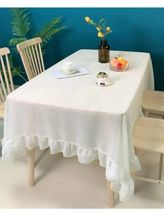 Detailed view of white Nordic tablecloth with ruffle edge on a wooden dining table